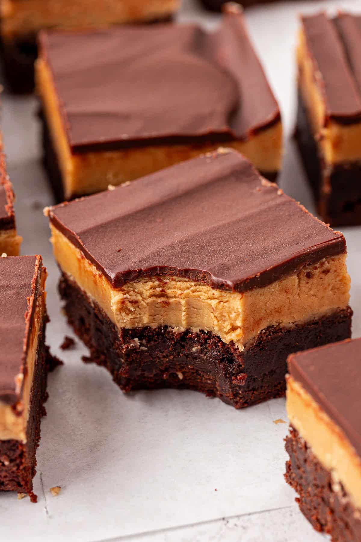 A close-up of chocolate and peanut butter layered buckeye brownies, with one piece showing a bite taken out, revealing thick layers of fudgy brownie, creamy peanut butter, and smooth chocolate topping.