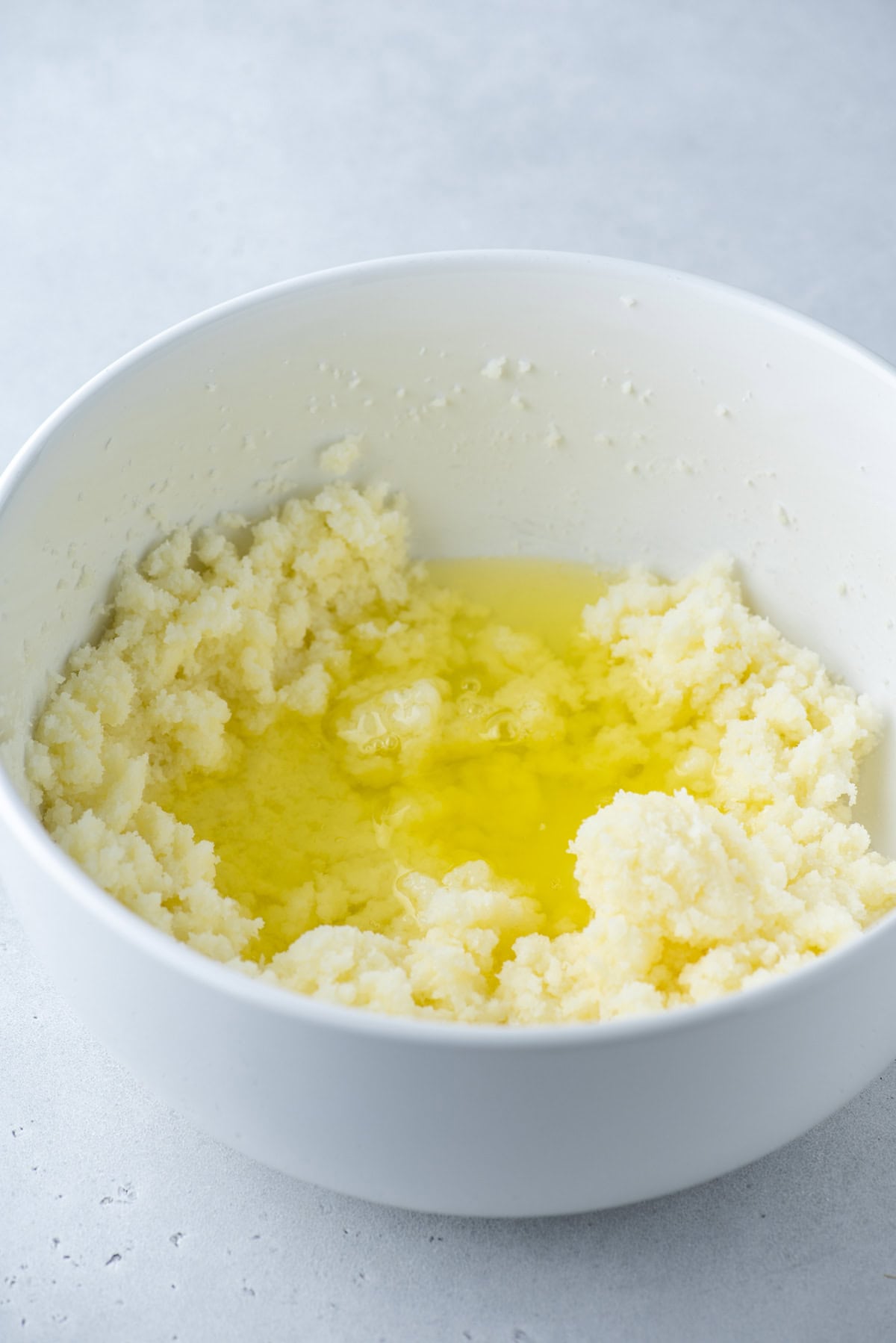 A white bowl containing creamed butter and sugar, with melted butter pooling in the center, sits on a light gray surface.