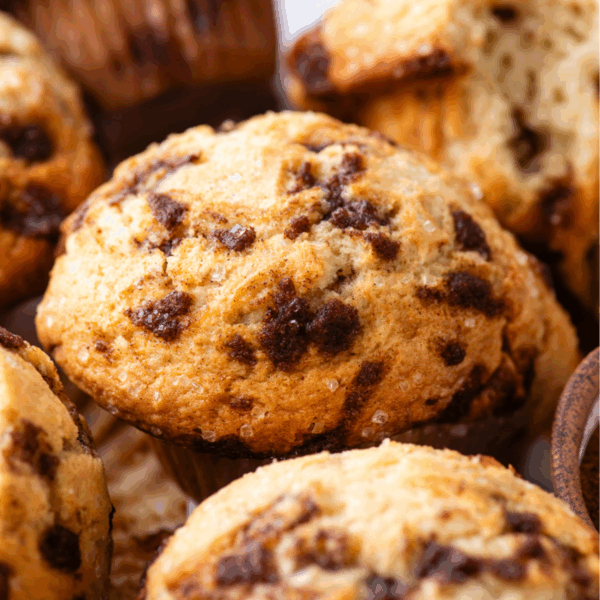 A close-up of golden-brown muffins with cinnamon chip chunks, showing a moist texture and slightly crispy tops, grouped closely together.