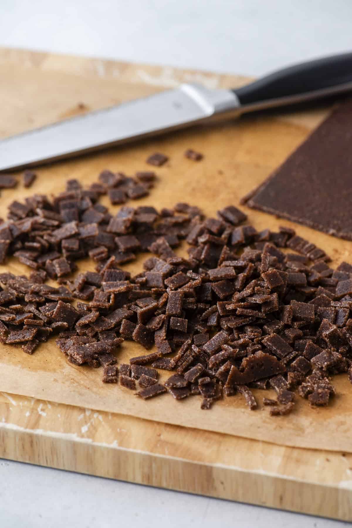 Small diced pieces of homemade cinnamon chips are scattered on a piece of parchment paper on a wooden cutting board, with a kitchen knife in the background.