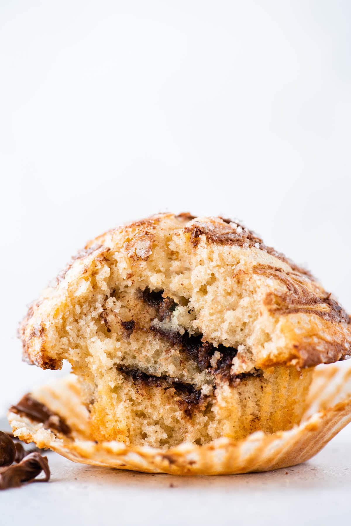 A close-up of a cinnamon swirl muffin, partially broken open to reveal its soft, fluffy interior with visible swirls of cinnamon filling, sitting on an unwrapped paper liner.