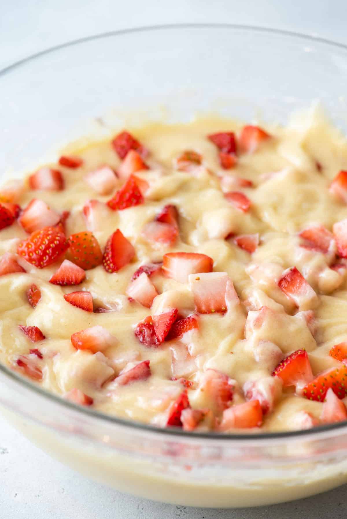A glass bowl filled with cake batter mixed with chopped fresh strawberries, ready to be baked.