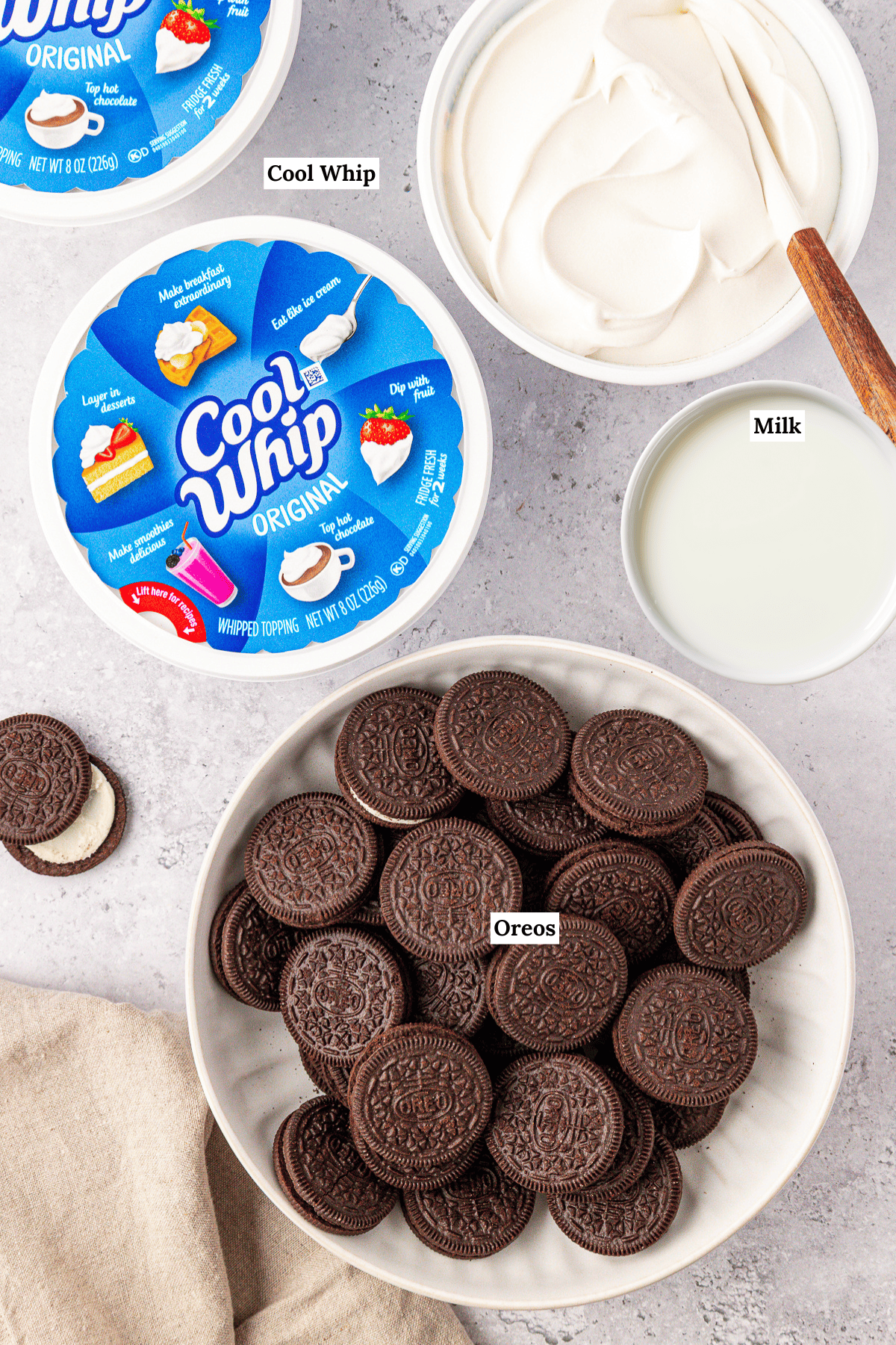 A bowl of whole Oreos, a bowl of Cool Whip whipped topping, and a bowl of milk sit on a countertop. Each item is labeled with text: Cool Whip, Milk, and Oreos.