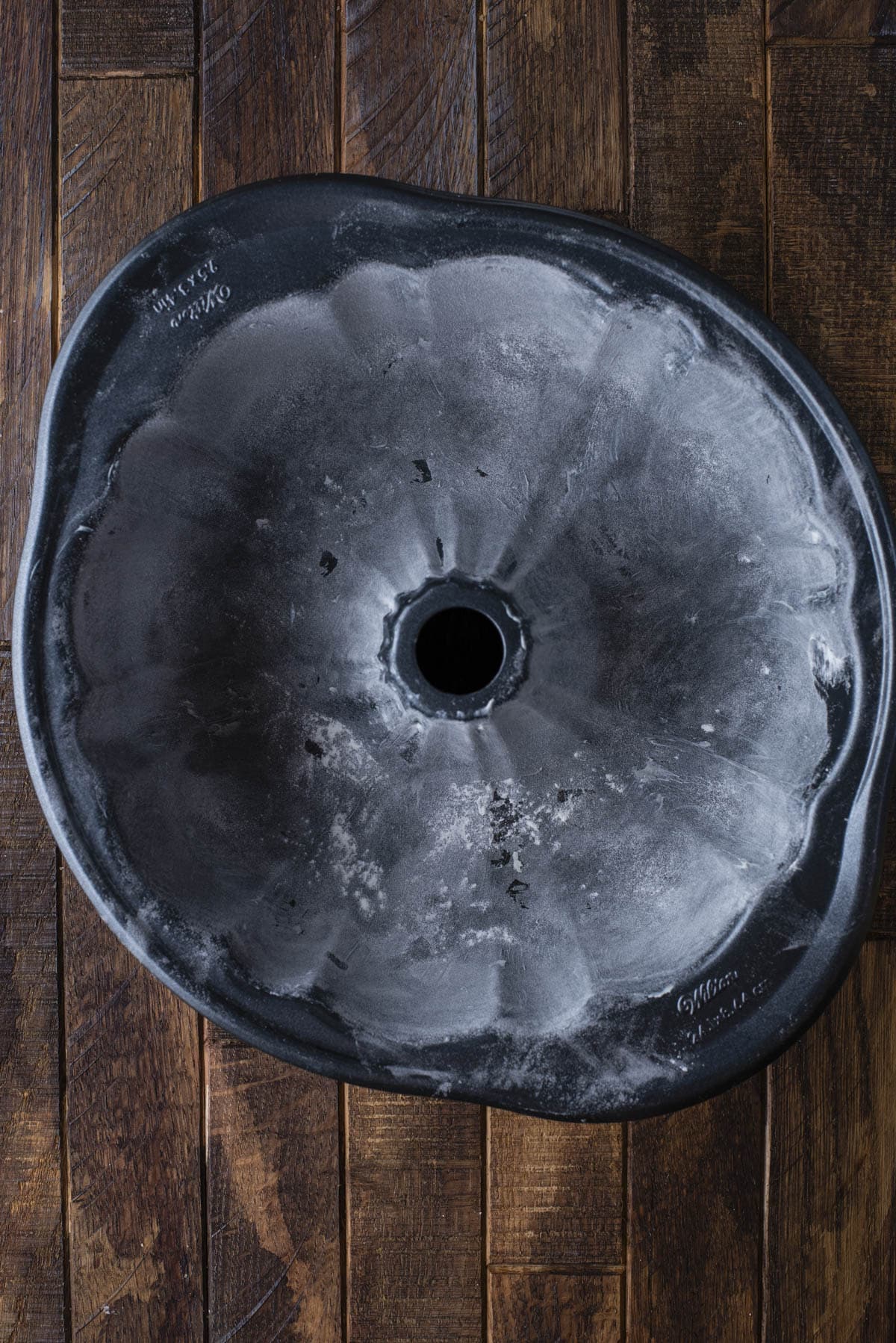 A top-down view of a flower-shaped bundt cake pan lightly dusted with flour, resting on a dark wooden surface.