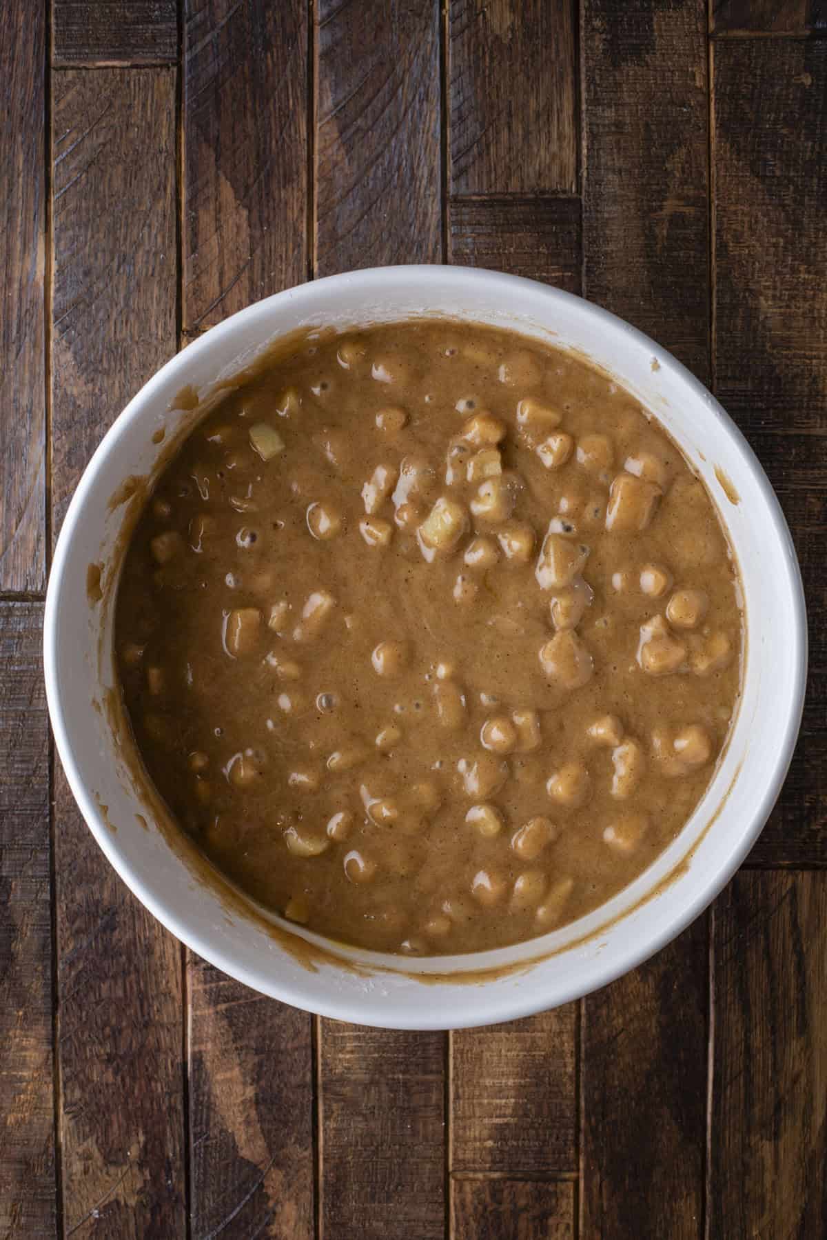 A white bowl filled with thick, chunky brown batter containing visible pieces, placed on a rustic dark wooden surface.