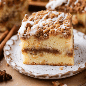 A slice of crumb-topped coffee cake with a cinnamon swirl filling and white icing drizzle, served on a speckled ceramic plate.