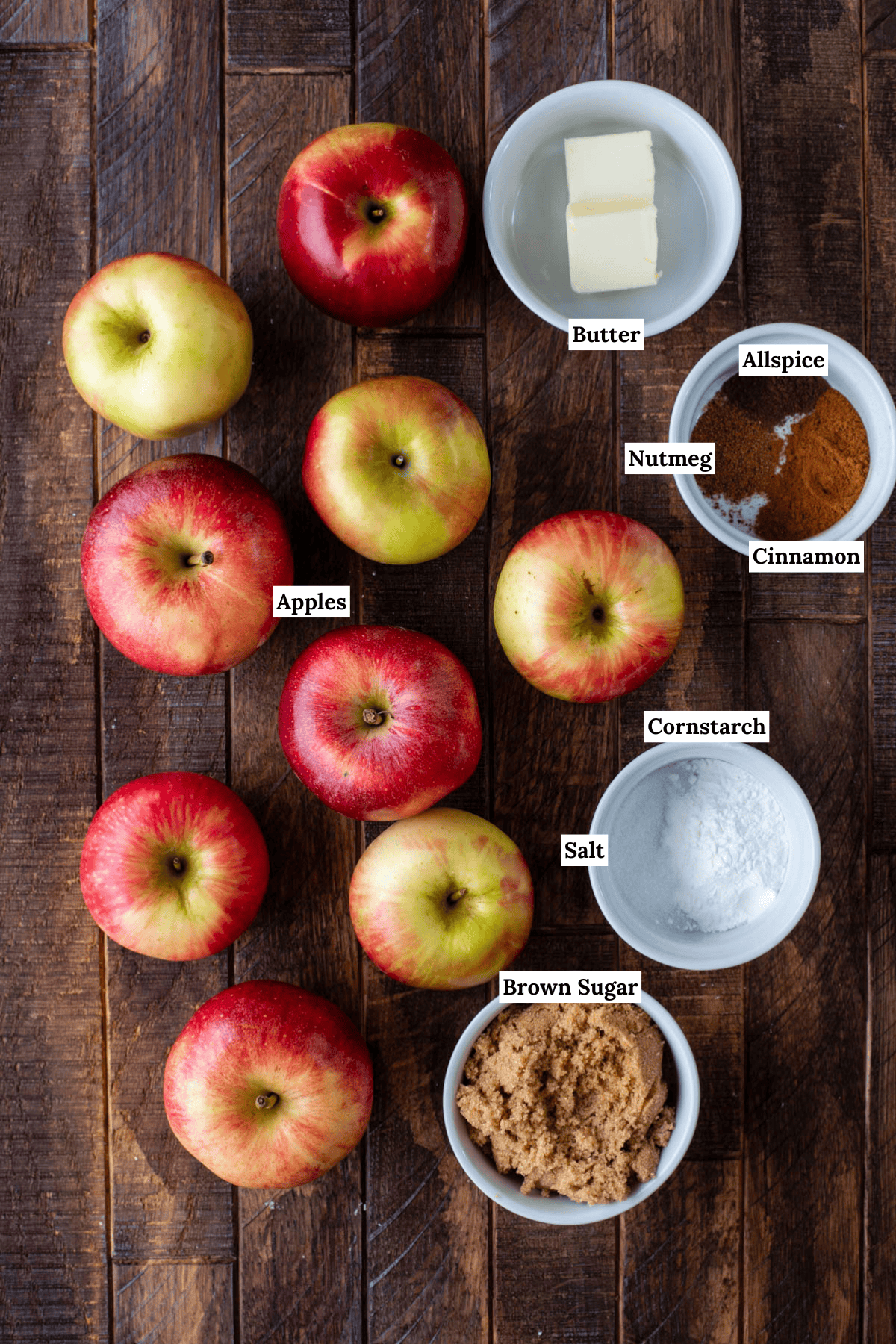 Apples and a few bowls of ingredients on a wood surface.