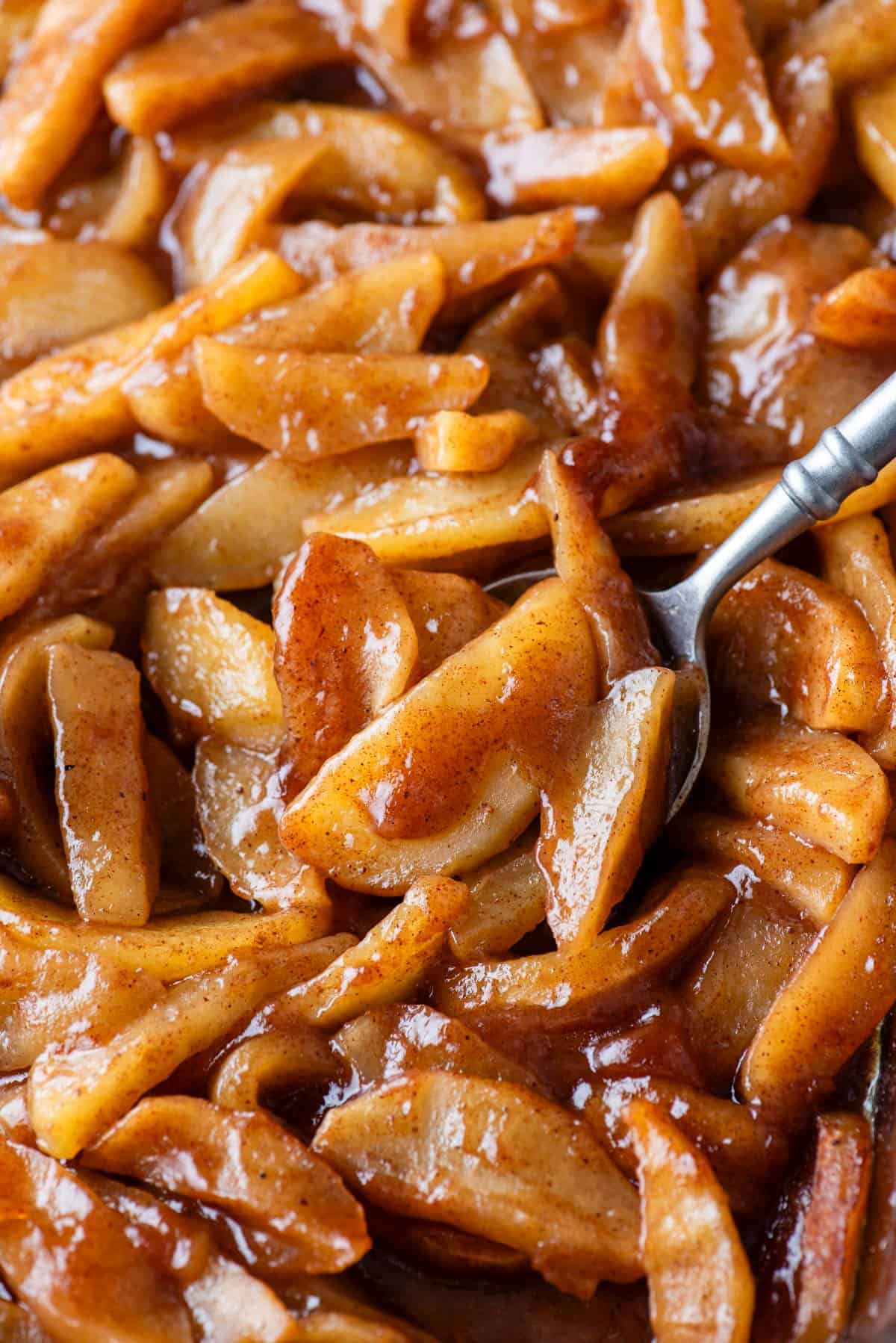 Close-up of caramelized apple slices coated in cinnamon and brown sugar, with a spoon scooping through the glossy, warm mixture.