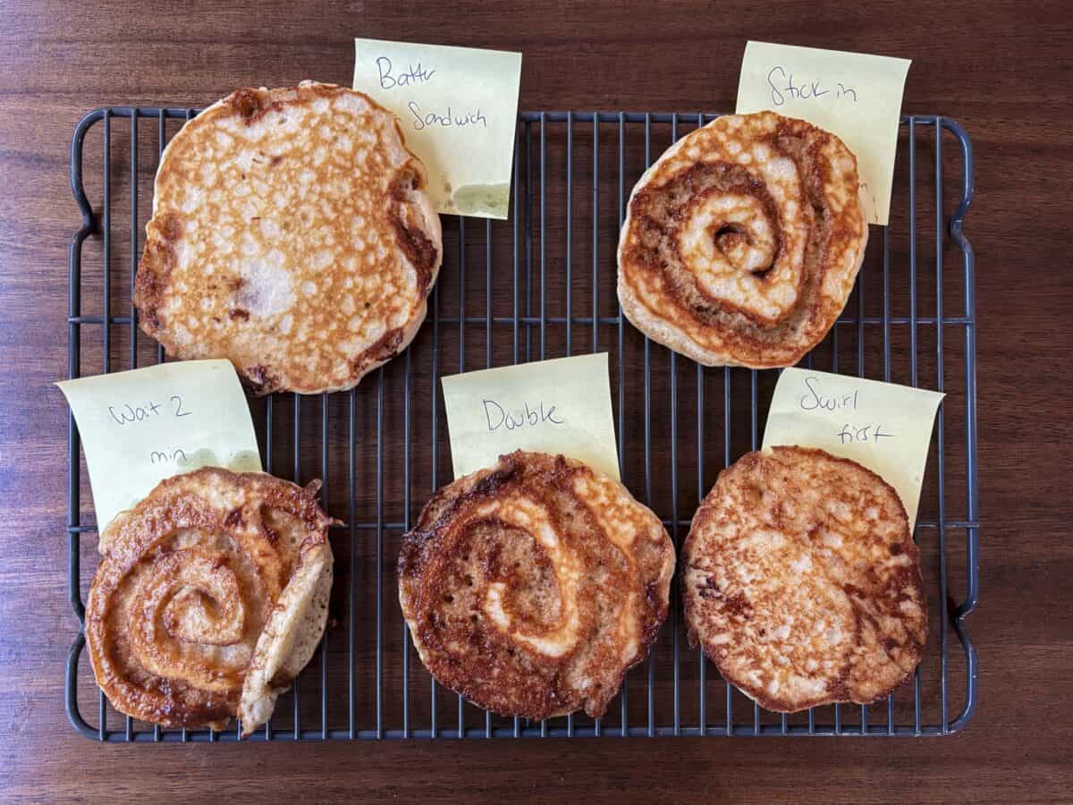 Five pancakes with various textures and swirl patterns are placed on a cooling rack, each labeled with a sticky note reading: Wait 2 min, Butter Sandwich, Double, Stack in, and Swirl first.