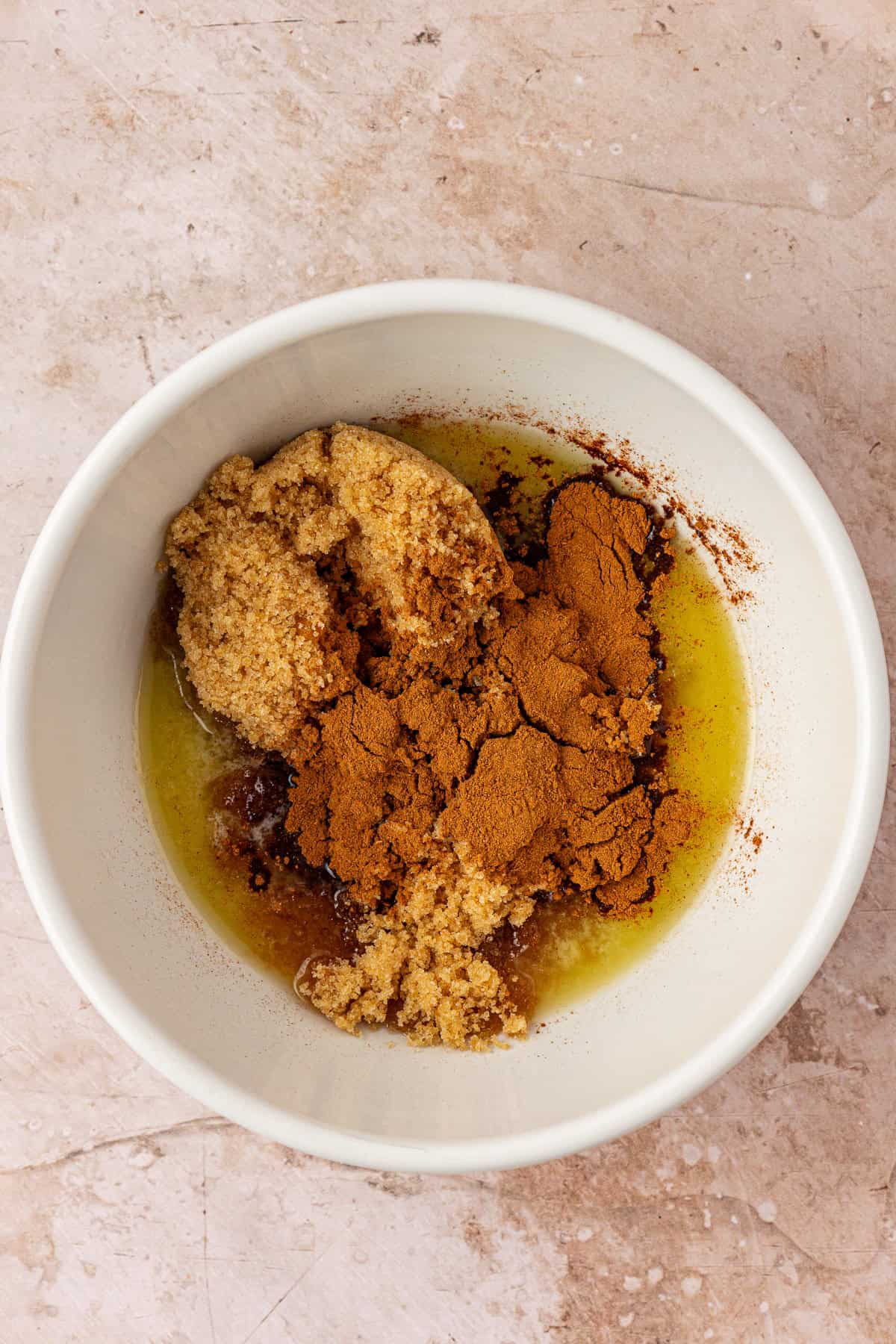 A white bowl containing melted butter, brown sugar, and ground cinnamon sits on a light-colored countertop.