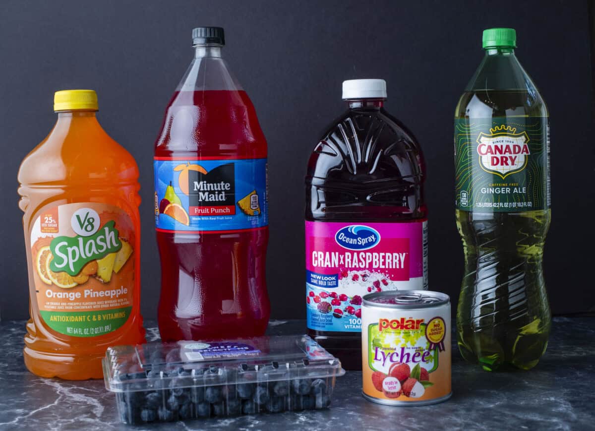 Assorted beverages and fruits including a V8 Splash Orange Pineapple juice, Minute Maid Fruit Punch, Ocean Spray Cran-Raspberry juice, Canada Dry Ginger Ale, blueberries, and a can of Polar lychee.