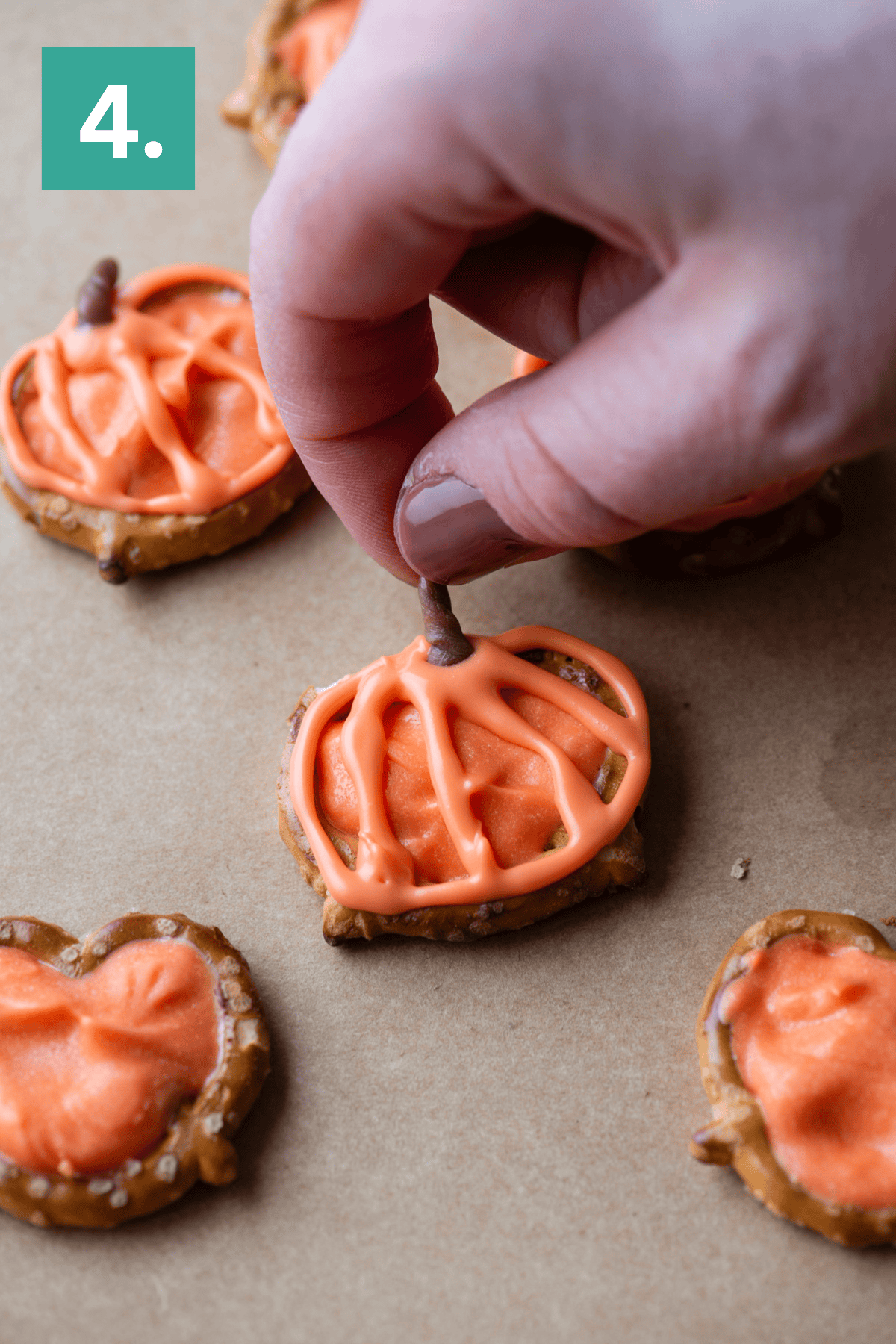 A hand holding a finger over a pretzel with orange frosting.