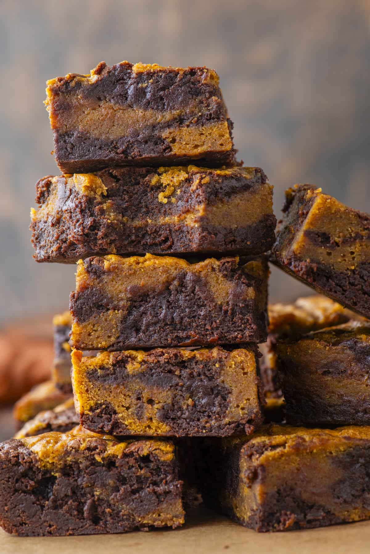 A stack of pumpkin swirl brownies, showing layers of rich, dark chocolate brownie and orange pumpkin filling, against a blurred neutral background.