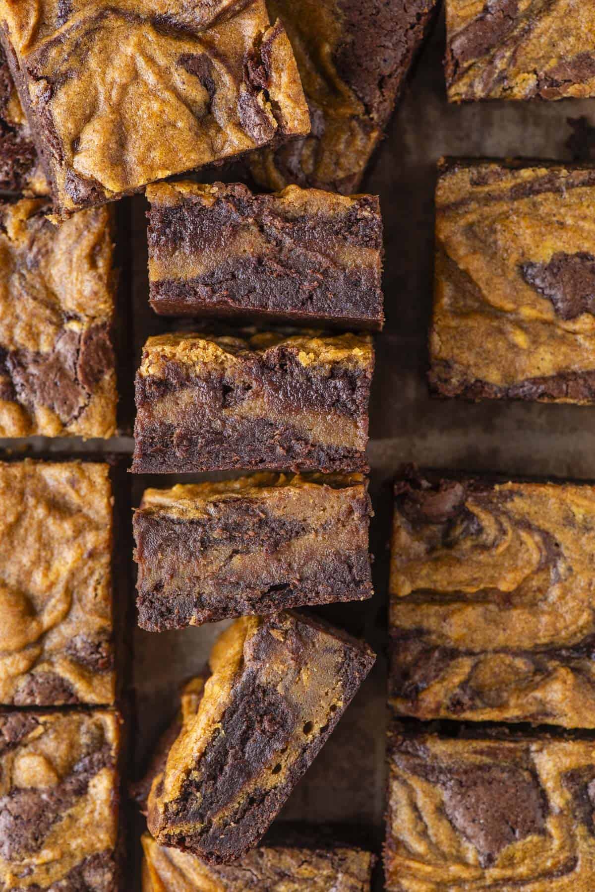 Overhead view of several pumpkin swirl brownies, cut into squares. The brownies have a marbled pattern with rich brown chocolate and orange pumpkin swirls visible on the tops and sides.