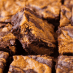 Close-up of several fudgy chocolate brownies swirled with a golden brown peanut butter layer, with one brownie positioned at an angle above the others.