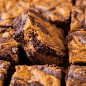 Close-up of several fudgy chocolate brownies swirled with a golden brown peanut butter layer, with one brownie positioned at an angle above the others.