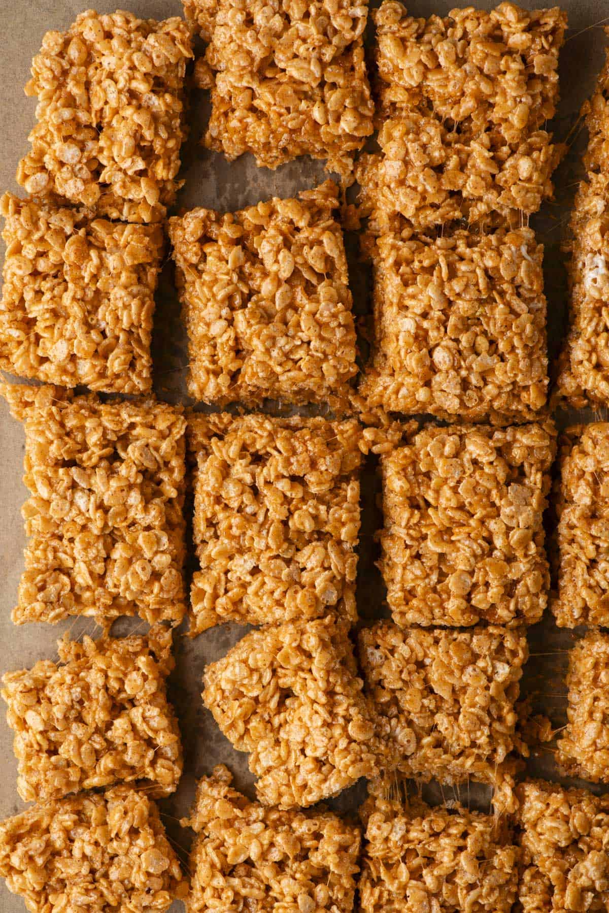 Close-up of several square Rice Krispies treats arranged in rows on parchment paper, showing their crispy, golden-brown texture and slightly sticky appearance.