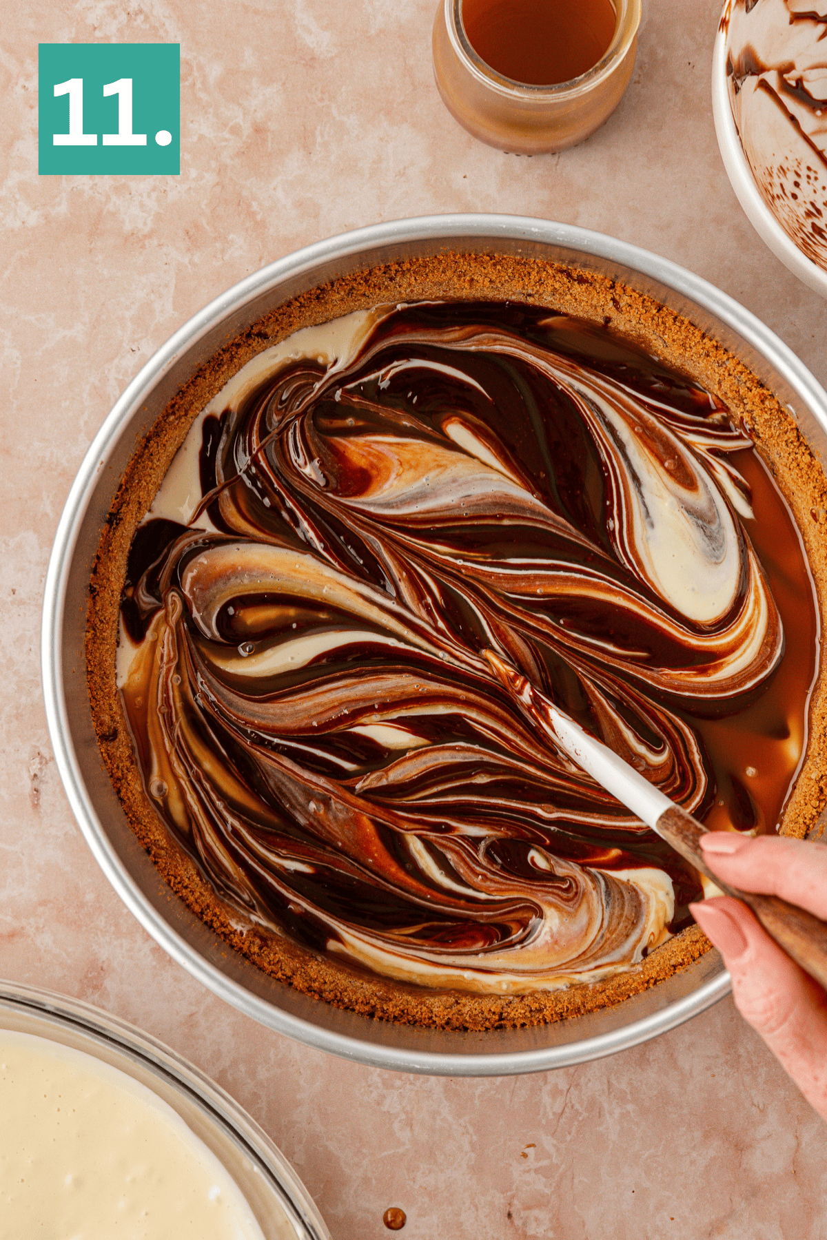 A hand swirls chocolate and caramel into a creamy pie filling in a round crust, creating a marbled pattern. A small jar of caramel and a bowl with remaining filling sit nearby. The image is labeled 11. in a green box.
