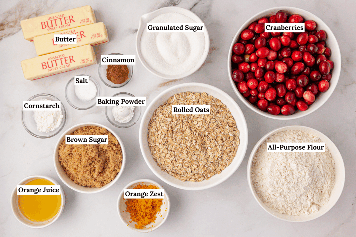 overhead view of the ingredients for cranberry crumb bars including three sticks of butter, cinnamon, salt, cornstarch, baking powder, granulated sugar, cranberries, rolled oats, brown sugar, orange juice, orange zest, and all-purpose flour