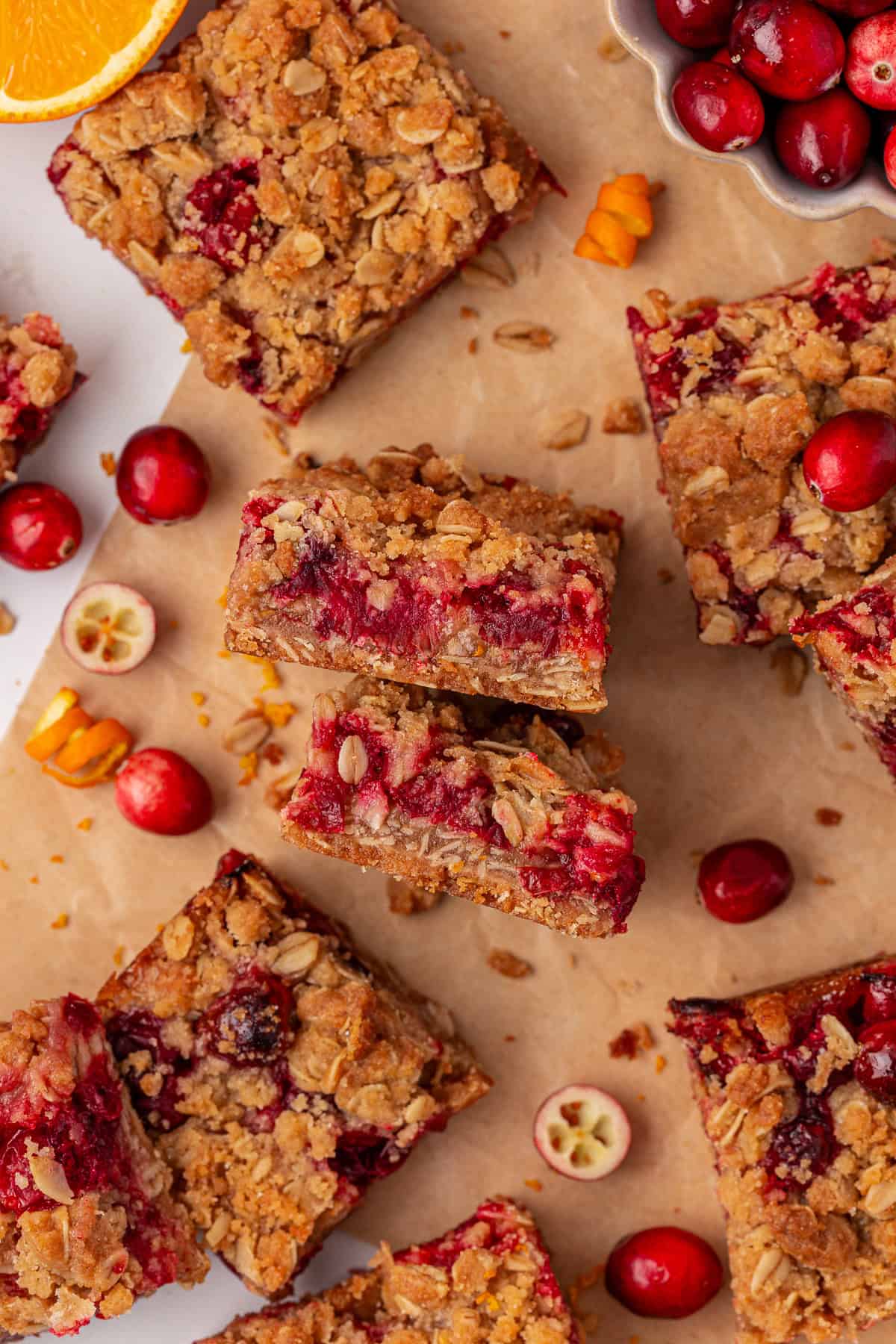 cranberry crumb bars scattered over brown parchment paper, some flat and some on their sides, surrounded by scattered cranberries and crumbs