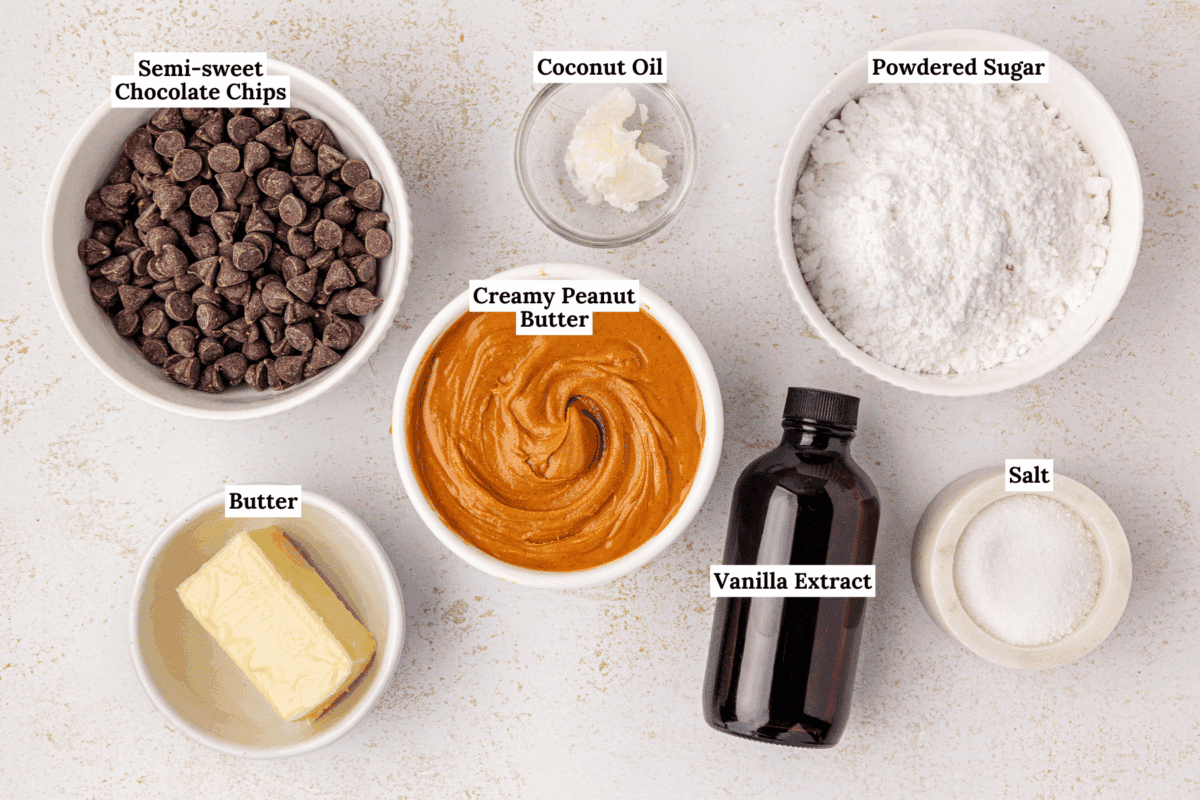 A top-down view of six labeled baking ingredients in bowls: semi-sweet chocolate chips, coconut oil, powdered sugar, creamy peanut butter, butter, vanilla extract, and salt.