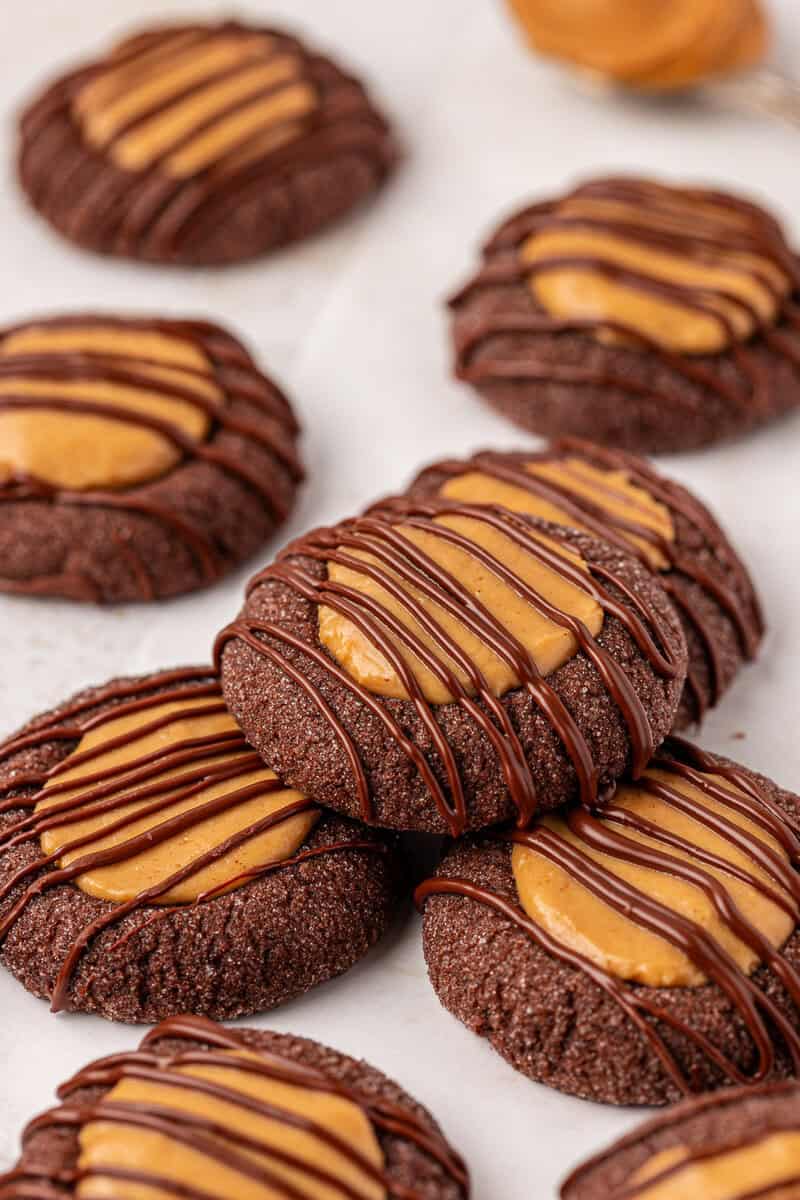 Chocolate cookies topped with a peanut butter filling and drizzled with chocolate, arranged on a light surface. The cookies appear soft and rich, with a glossy finish from the chocolate drizzle.