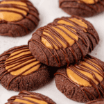 Chocolate cookies topped with a dollop of peanut butter and drizzled with melted chocolate, arranged closely together on a white surface.