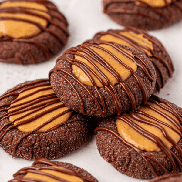 Chocolate cookies topped with a dollop of peanut butter and drizzled with melted chocolate, arranged closely together on a white surface.