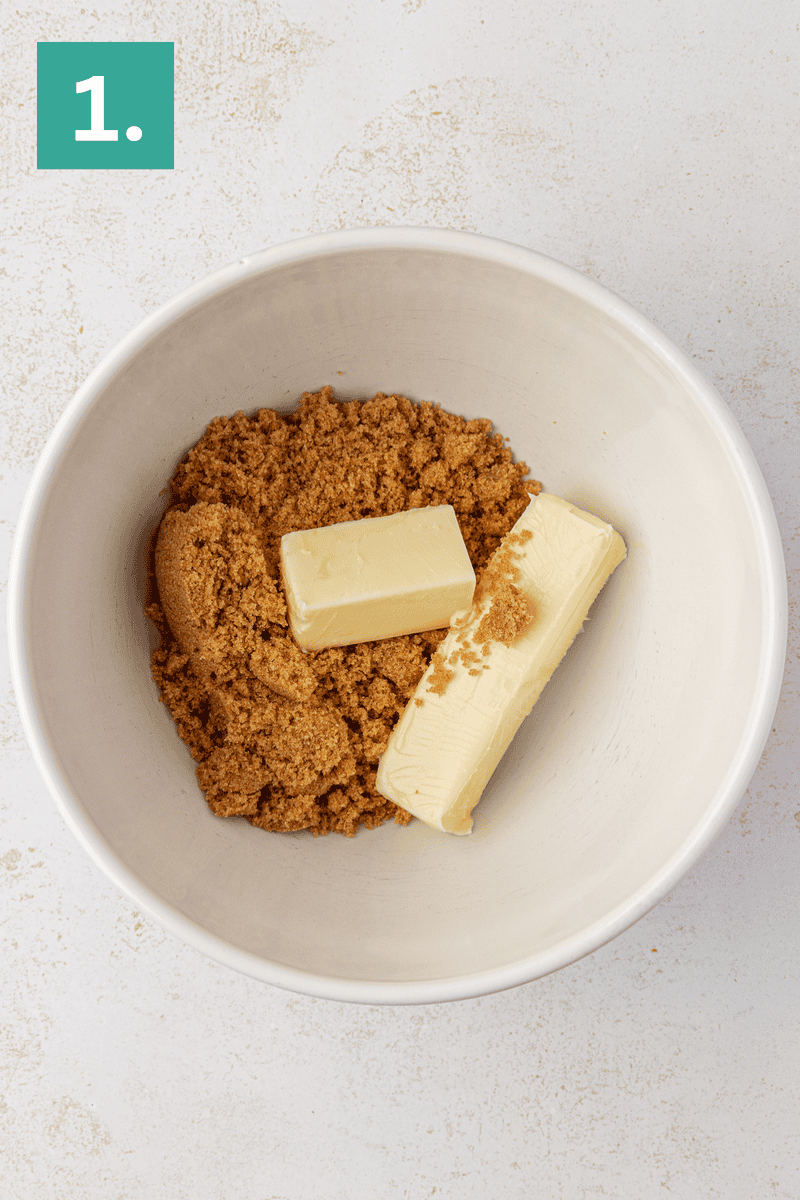 A white bowl contains two sticks of butter and brown sugar. In the top left corner, a green square with the number 1 is displayed. The bowl is set on a light-colored surface.