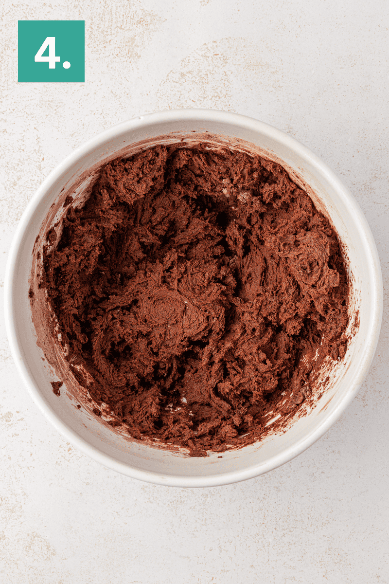A white mixing bowl filled with chocolate cookie dough sits on a light surface. In the top left corner, a green box with the number 4 in white indicates the step in a recipe process.