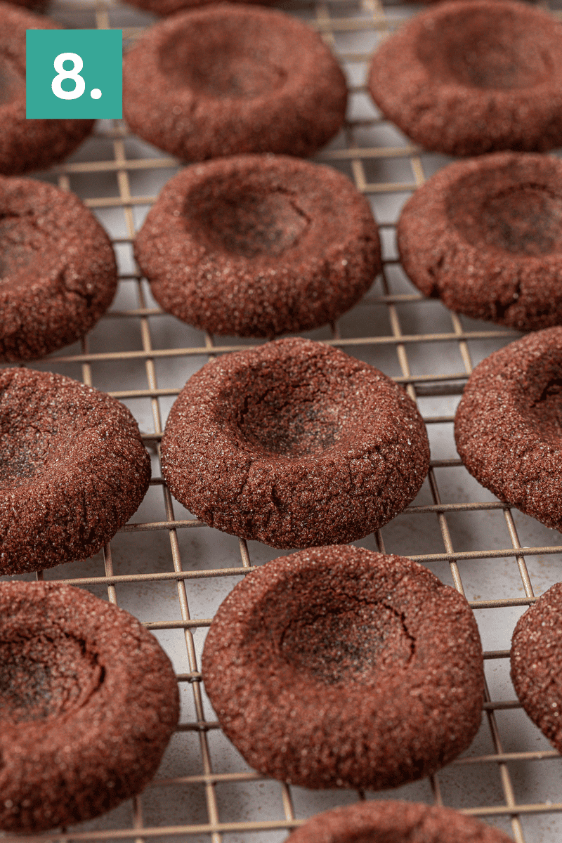 Chocolate thumbprint cookies cooling on a wire rack, each with a circular indentation in the center. A green square in the top left corner shows the number 8 in white.