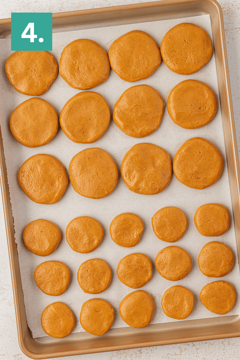A baking tray lined with parchment paper holds rows of unbaked, round, orange-brown dough discs. A green box labeled “4.” is in the top left corner.