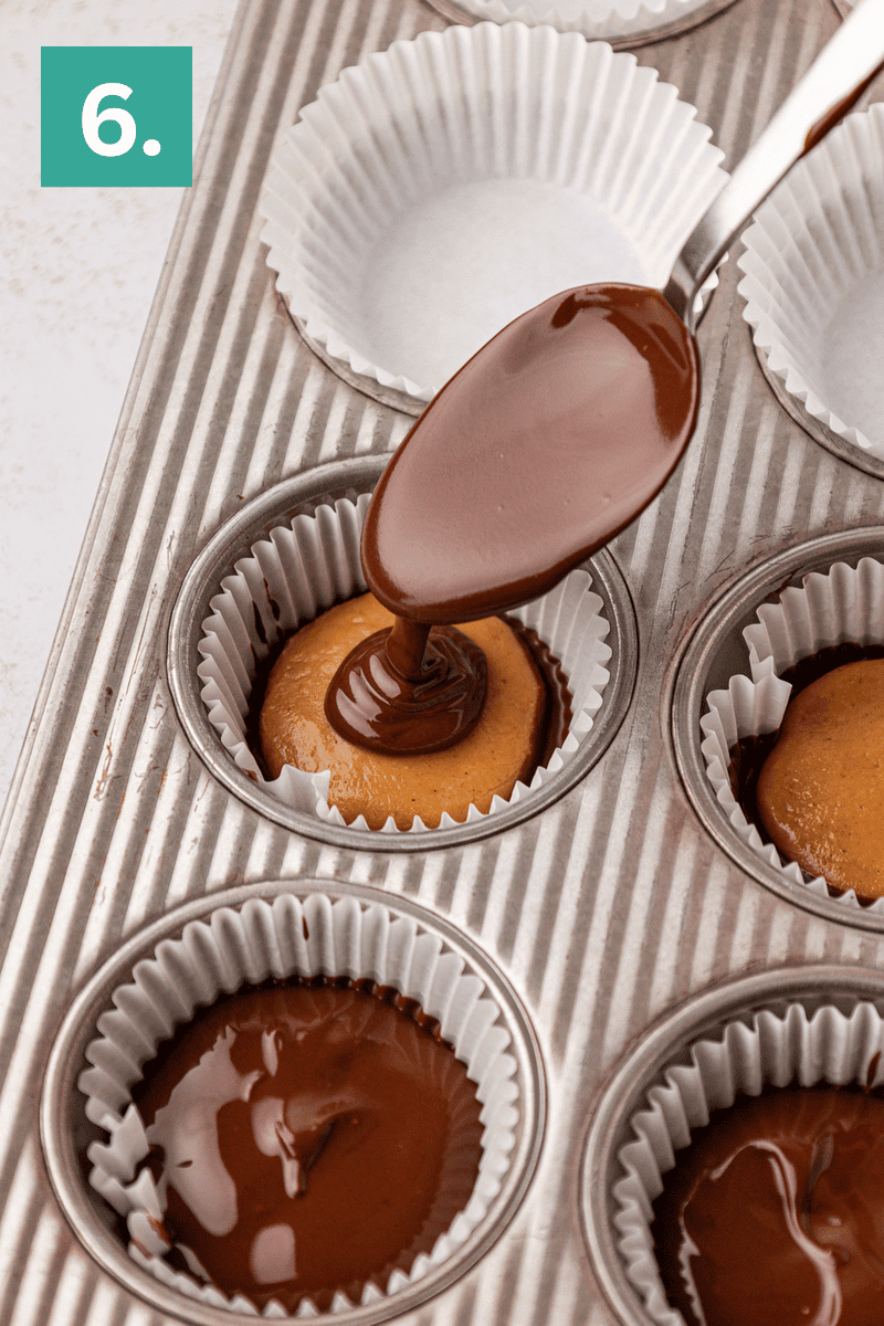 A spoon pours melted chocolate over peanut butter filling in a cupcake liner inside a muffin tin, with a green square labeled “6” in the corner.