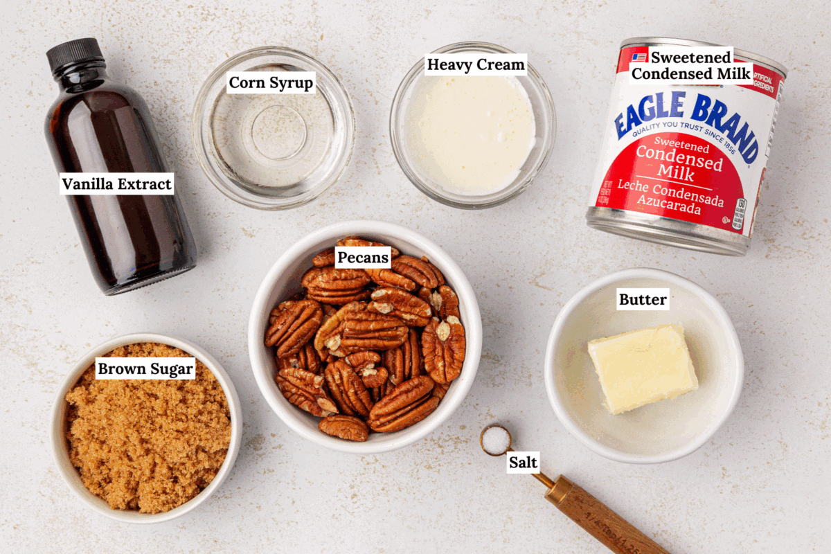 Top-down view of measured ingredients for a recipe: vanilla extract, corn syrup, heavy cream, sweetened condensed milk, brown sugar, pecans, butter, and salt, each labeled with its name.