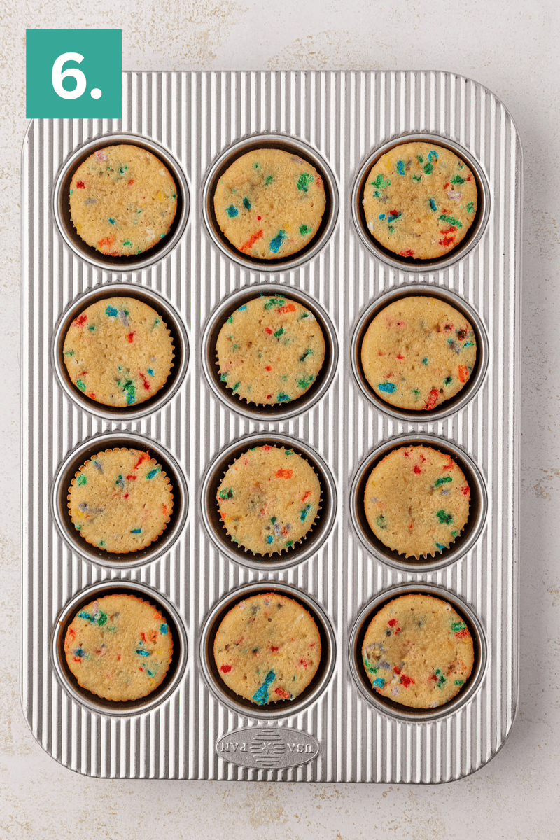A muffin tin filled with twelve paper liners, each holding raw cupcake batter with colorful sprinkles. A green square labeled 6. is in the top left corner.