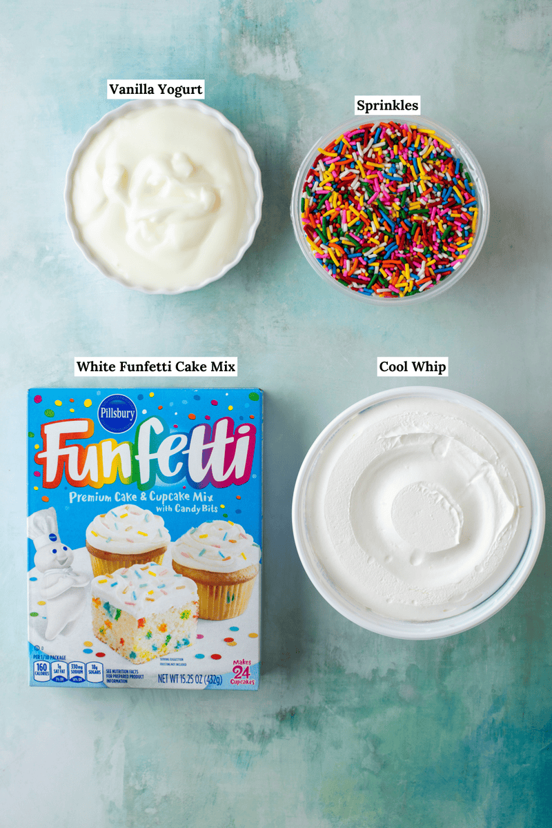 Four items arranged on a blue surface: a bowl of vanilla yogurt, a bowl of rainbow sprinkles, a tub of Cool Whip, and a box of Pillsbury Funfetti cake mix, each labeled with text.