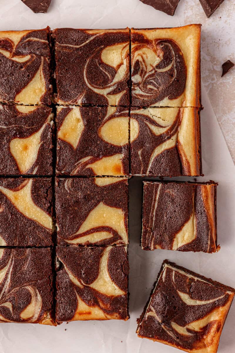 A tray of marble cheesecake brownies sliced into squares, showing a swirled pattern of cream cheese and chocolate on top.