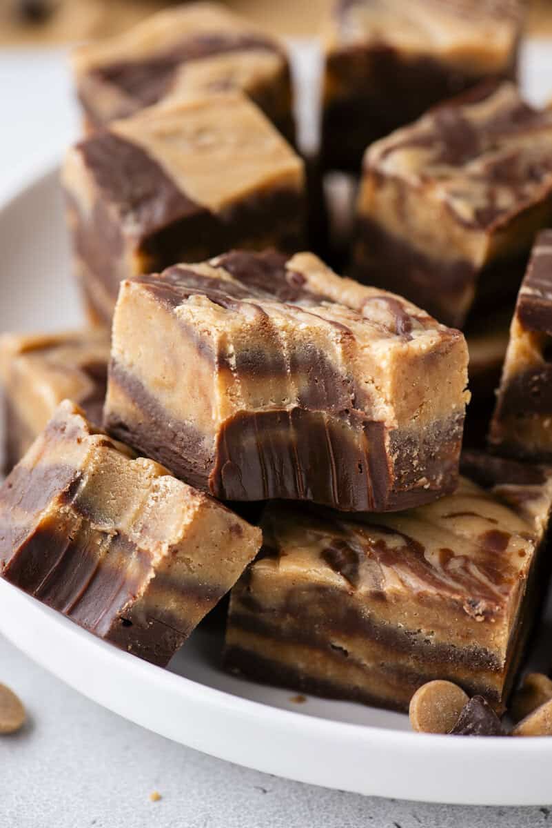 A close-up of several pieces of layered chocolate and peanut butter fudge stacked in a white bowl. The fudge has a marbled appearance with distinct swirls of brown and tan.