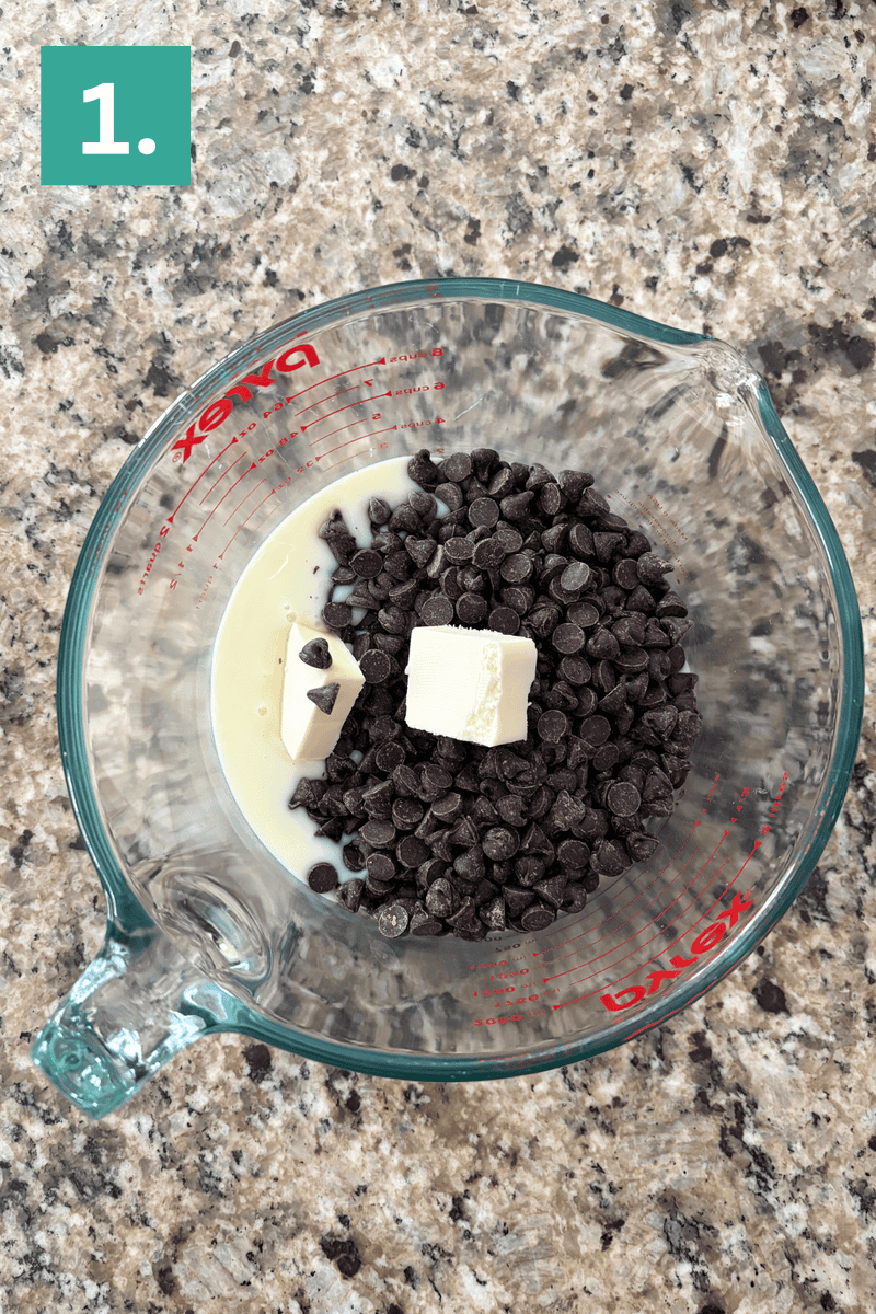 A glass measuring cup on a granite countertop contains chocolate chips, two chunks of butter, and sweetened condensed milk. A green box with a white number 1 is in the top left corner.