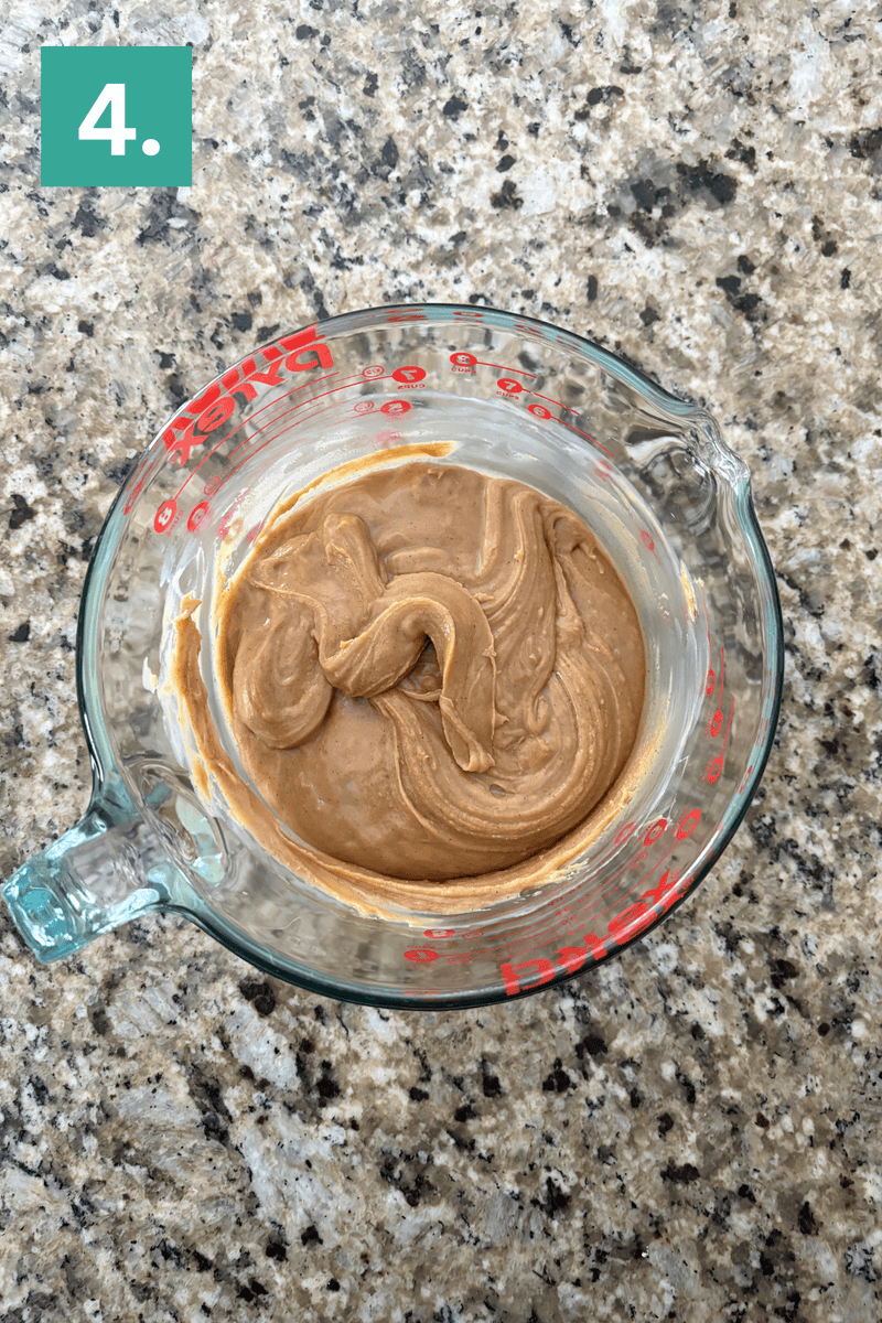 A glass measuring cup filled with a creamy, light brown mixture sits on a speckled countertop. A green box with the number 4 in white is in the top left corner.