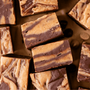 Several pieces of swirled chocolate and peanut butter fudge are arranged on a brown surface, showcasing their marbled layers and rich, creamy texture.