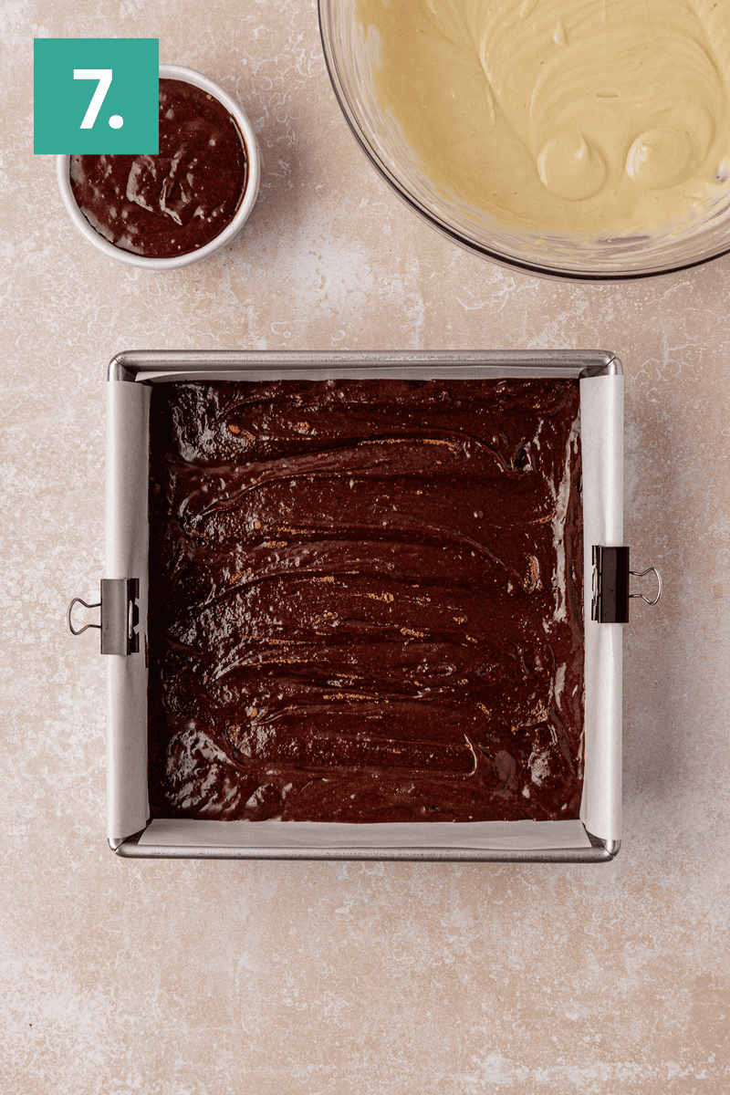 A square baking pan filled with chocolate batter, a bowl with light-colored batter, and a small bowl with chocolate mixture on a beige countertop. A green box with the number 7 is in the top left corner.
