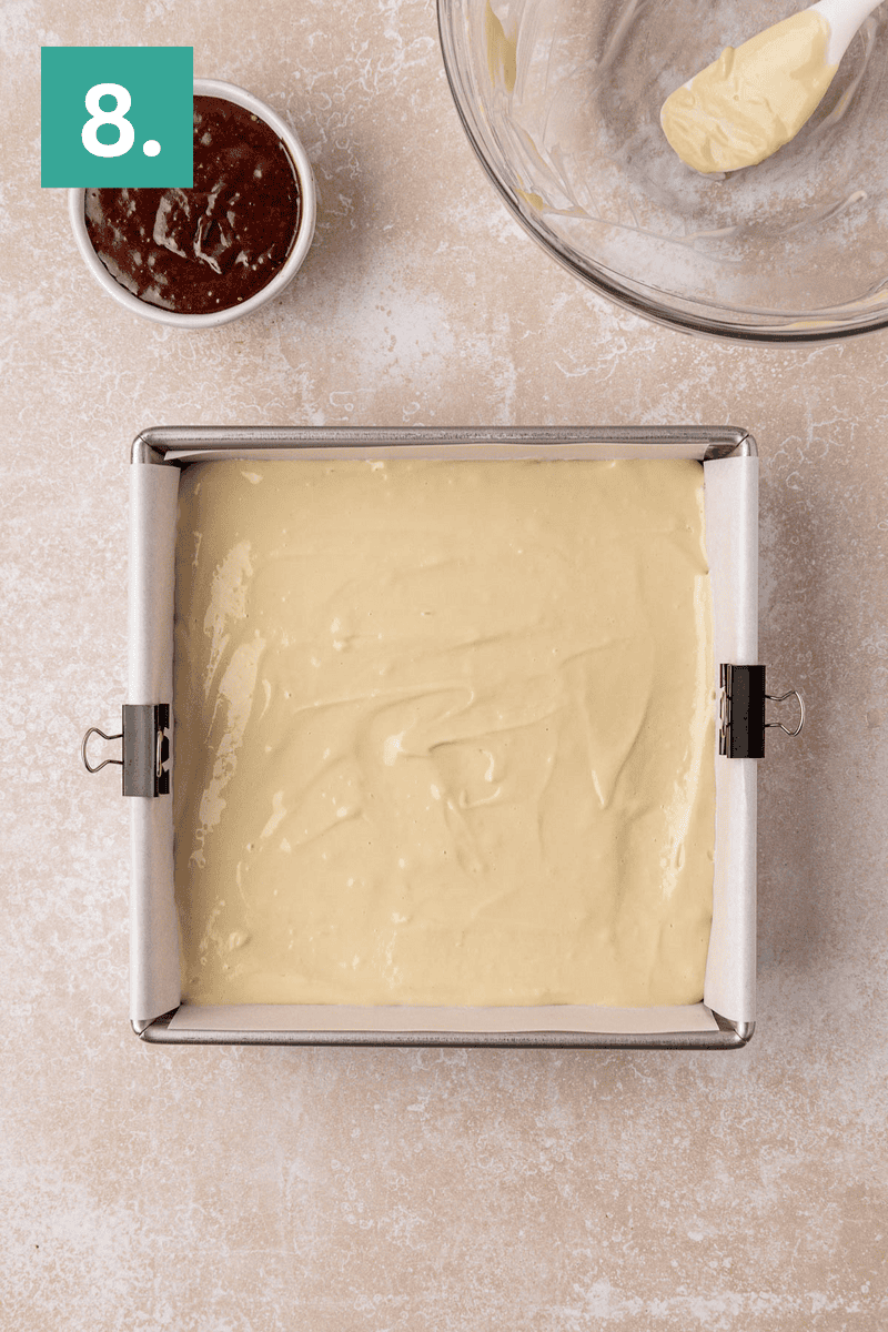 Overhead view of a square baking pan filled with smooth, light yellow cake batter. Nearby are a glass bowl with leftover batter and a small bowl of dark jam. A green box labeled 8. is in the top left corner.