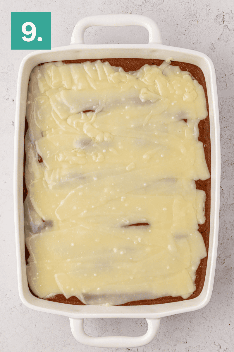 A rectangular white baking dish filled with a baked dessert topped with creamy white icing. The dish sits on a light-colored surface, and there is a green square with the number 9 in the top left corner.