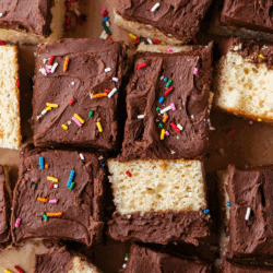 Overhead view of yellow cake squares topped with chocolate frosting and colorful sprinkles, arranged closely together. Text at the bottom reads: Box Cake Mix Hacks: How to Make Box Cake Better.