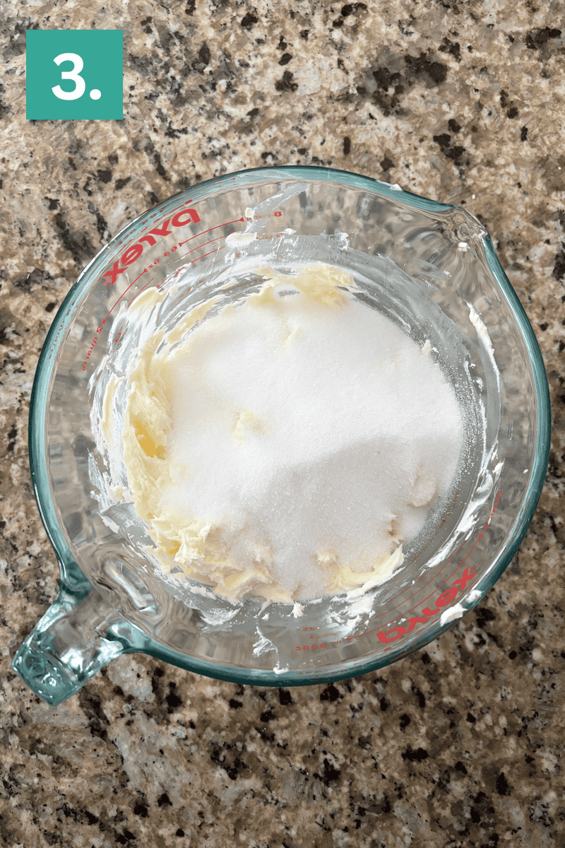 A glass measuring cup containing softened butter and sugar sits on a granite countertop. A green box with the number 3 is in the upper left corner, indicating step three of a recipe.