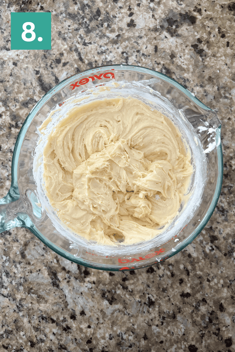 A glass measuring cup filled with creamy, mixed batter sits on a granite countertop. A green box with the number 8. is in the top left corner.