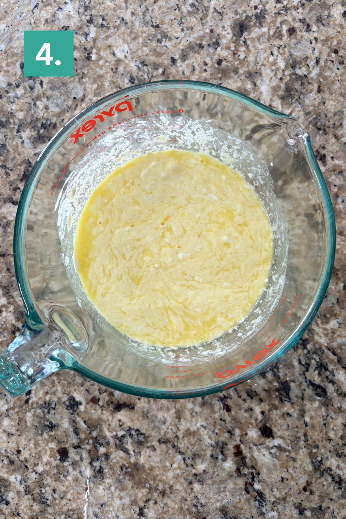 A glass measuring cup with a yellow, slightly lumpy batter mixture sits on a granite countertop. A green box with the number 4 is in the upper left corner of the image.