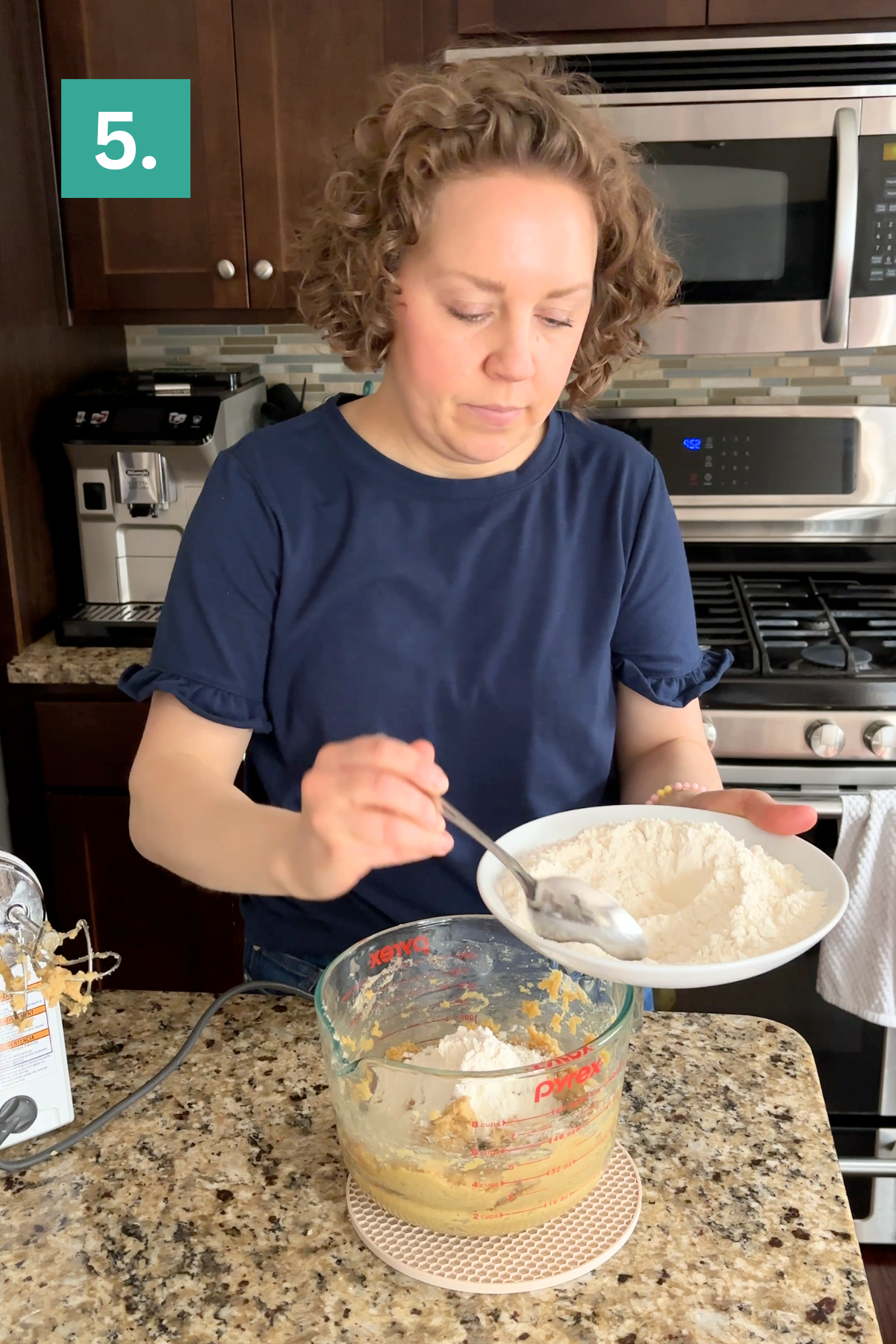 A woman stands in a kitchen, holding a plate of flour and spooning it into a measuring cup with batter—perfect for bakery style chocolate chip cookies. A green box with 5. appears in the top left, marking the fifth step in the recipe.