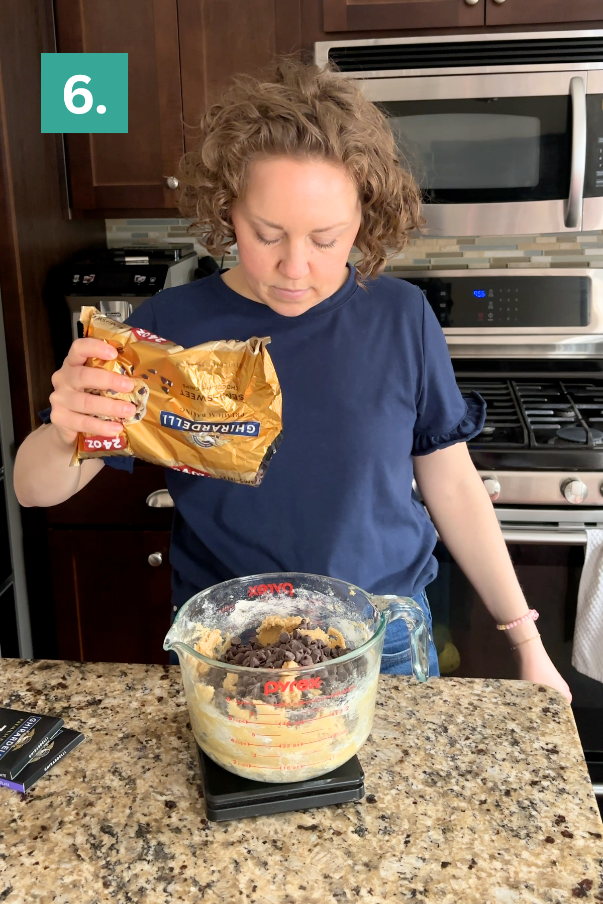 A woman stands in a kitchen pouring chocolate chips from a bag into a glass mixing bowl with cookie dough, preparing bakery style chocolate chip cookies. A green box with the number “6.” is in the top left corner.